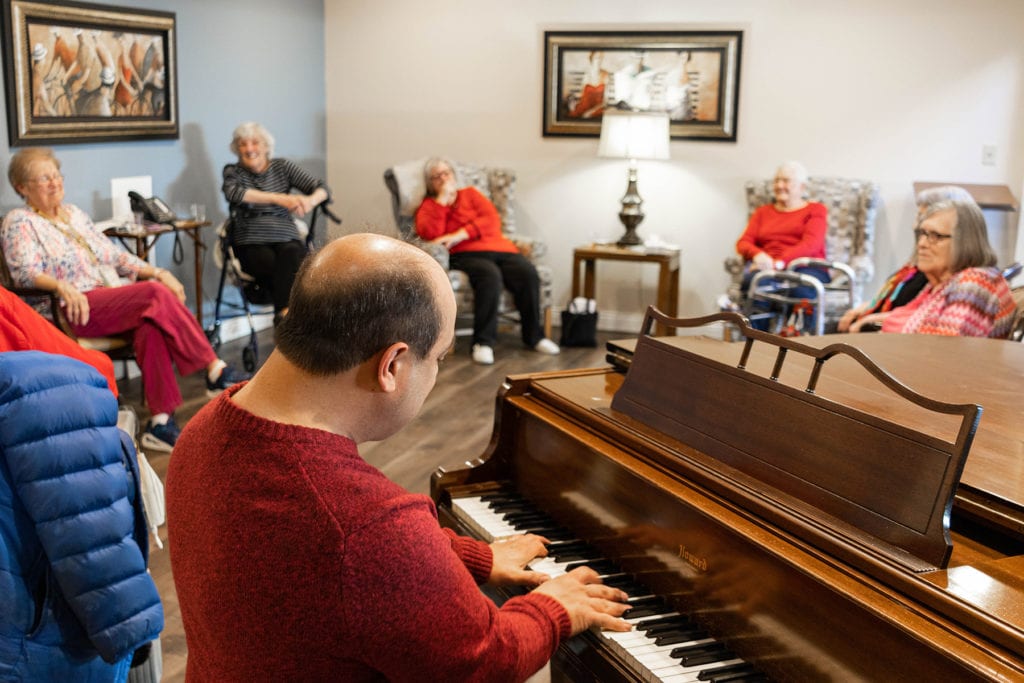 Senior community gather around the piano to listen to the music